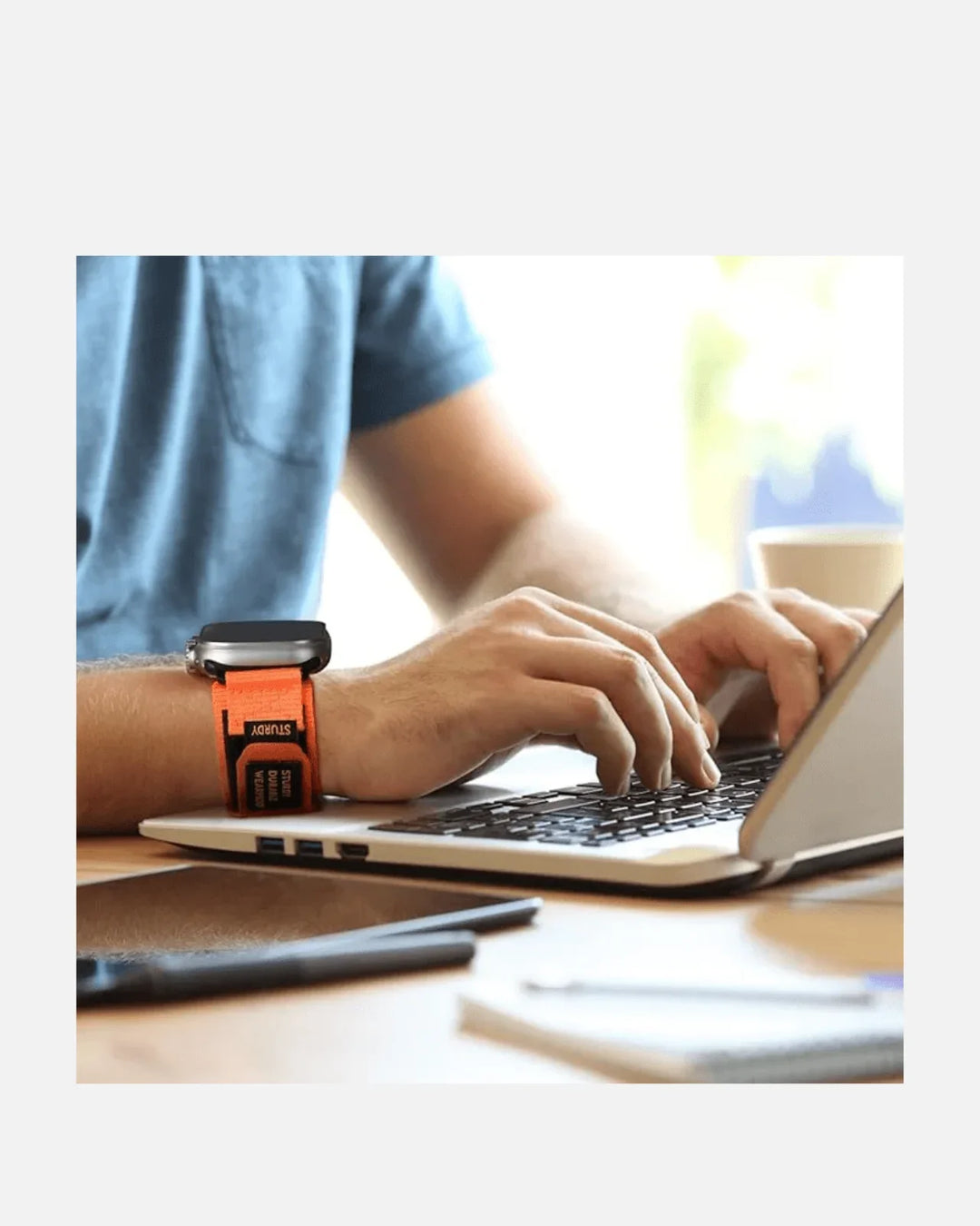Person typing on a laptop wearing a rugged orange nylon band for Apple Watch.
